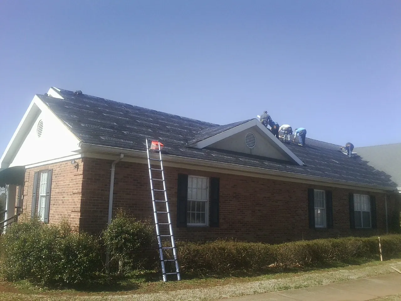 Crew tearing shingles off a brick ranch roof with a ladder set — Metal Roof Repair work by our crew in Saint Marys City