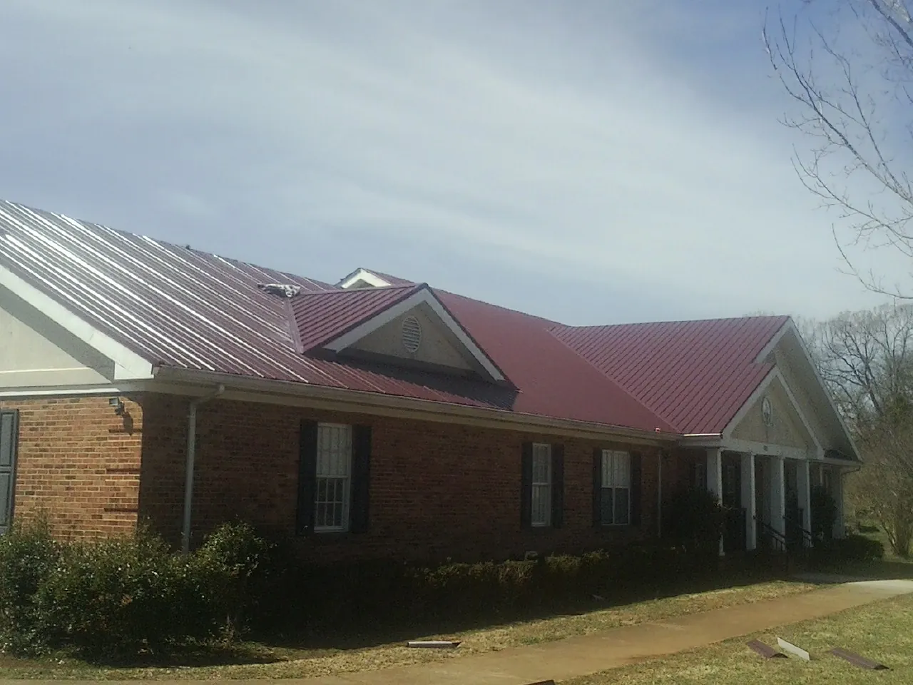 Red metal roof with gabled entries on a long brick building, from a Hail Damage Roof Repair job in Saint Marys City