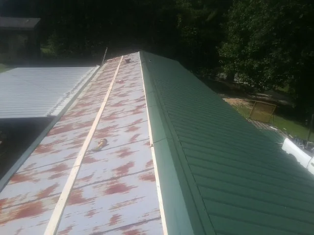 Old rusted panels beside newly installed green metal roofing — Wind Damage Roof Repair by Roofing Brothers in Saint Marys City