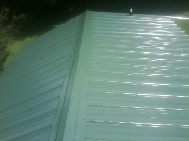 New green metal panels meeting at the ridge of a roof — Flat Roof Repair work by our crew in Saint Marys City