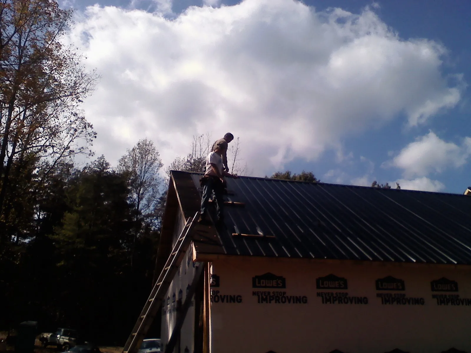 Roofer fastening dark metal panels high against a cloudy sky, from a Roof Inspection job in Saint Marys City
