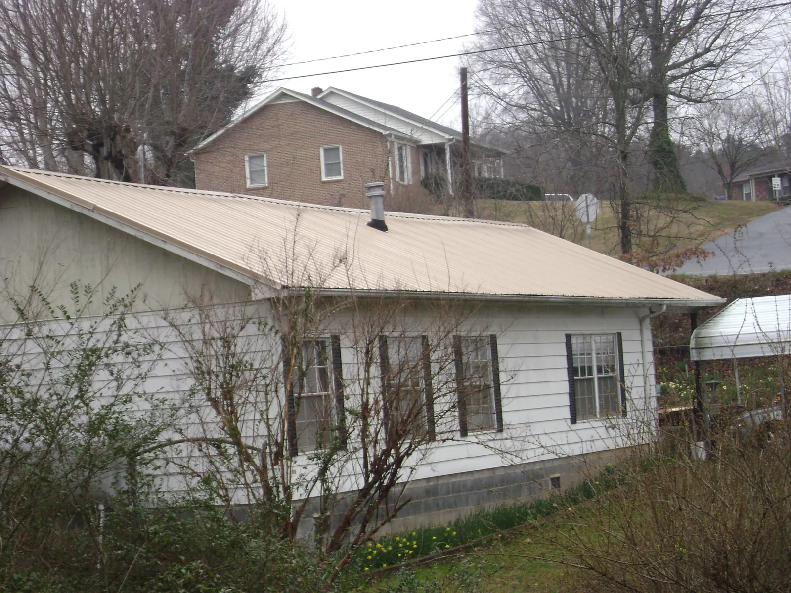 Tan metal roof on a white sided house set into a hillside — Commercial Roofing by Roofing Brothers in Saint Marys City