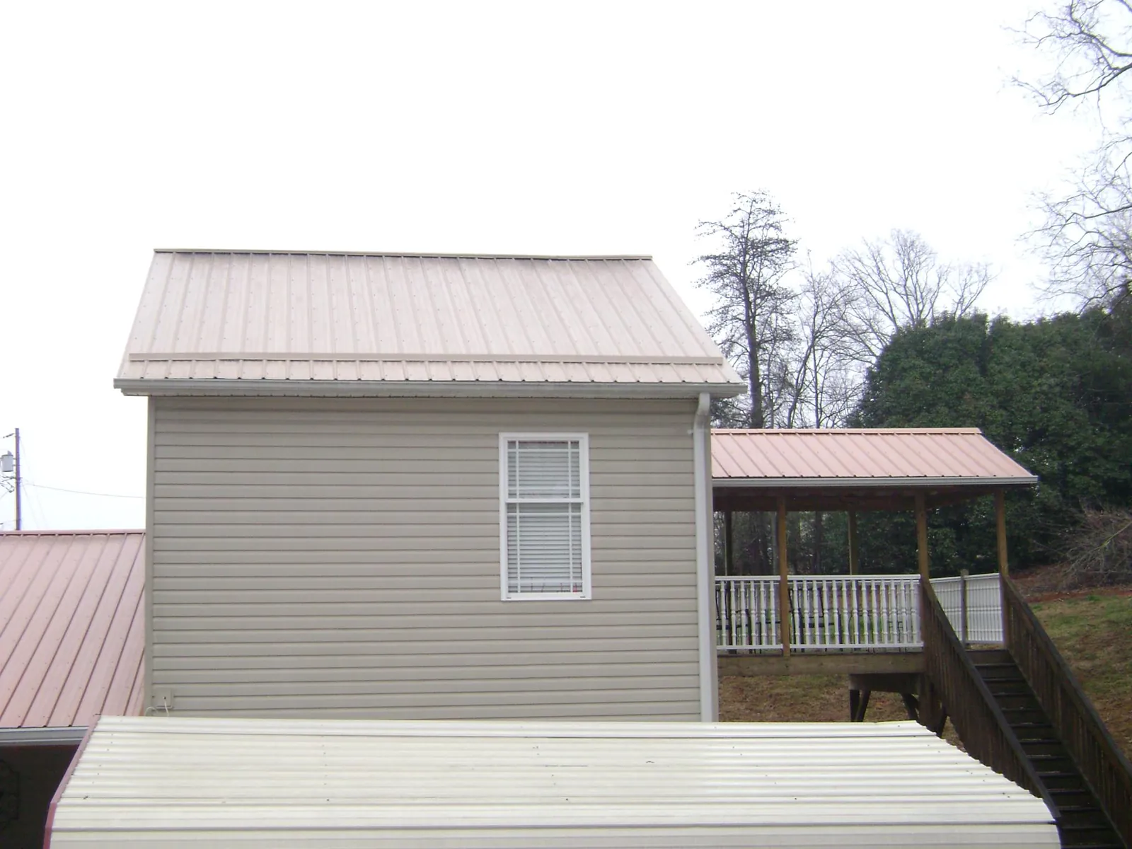 Tan metal roofs on a two story addition and attached porch, from a Roof Replacement job in Saint Marys City